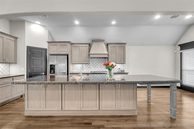 kitchen featuring visible vents, a spacious island, vaulted ceiling, custom range hood, and stainless steel fridge