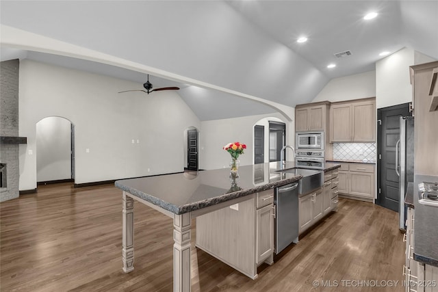 kitchen featuring a center island with sink, arched walkways, ceiling fan, stainless steel appliances, and vaulted ceiling