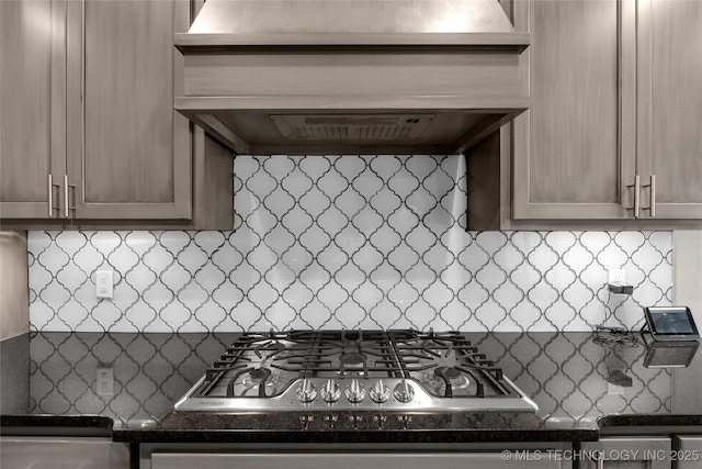 kitchen featuring decorative backsplash, dark countertops, premium range hood, and stainless steel gas cooktop