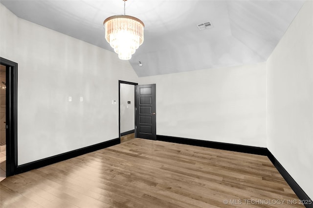 empty room featuring visible vents, baseboards, lofted ceiling, wood finished floors, and a notable chandelier