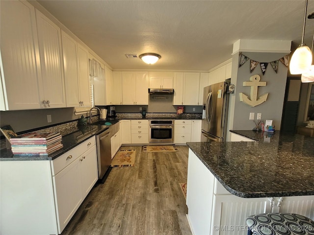 kitchen featuring dark wood finished floors, under cabinet range hood, a peninsula, stainless steel appliances, and a sink