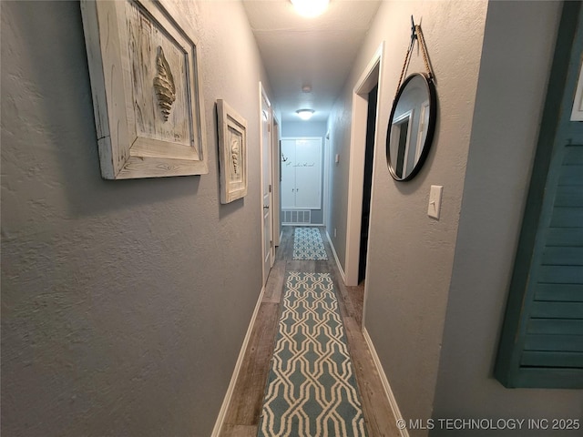 hallway featuring baseboards, wood finished floors, and a textured wall