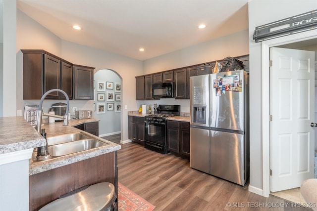 kitchen with black appliances, wood finished floors, dark brown cabinetry, and a sink