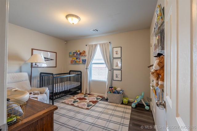 bedroom with visible vents, a crib, baseboards, and wood finished floors