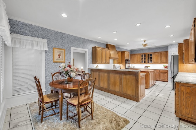 kitchen featuring light tile patterned floors, brown cabinets, a peninsula, and freestanding refrigerator