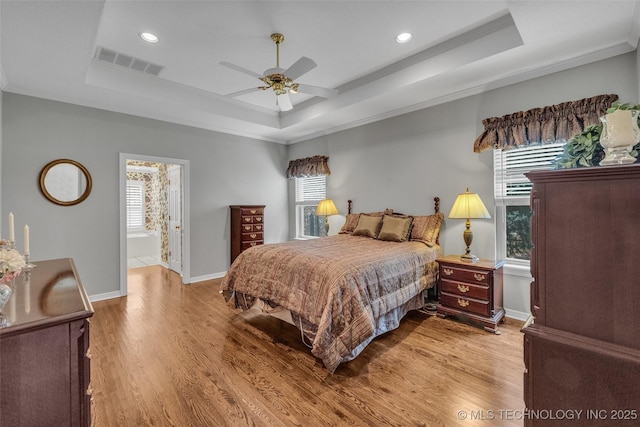 bedroom with a raised ceiling, wood finished floors, and visible vents