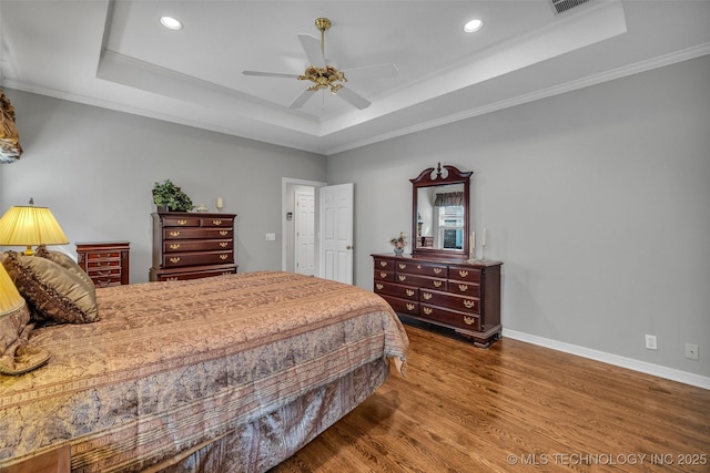 bedroom featuring baseboards, a raised ceiling, wood finished floors, and ornamental molding