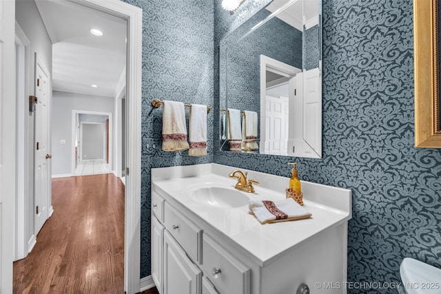 half bathroom featuring wallpapered walls, wood finished floors, and vanity