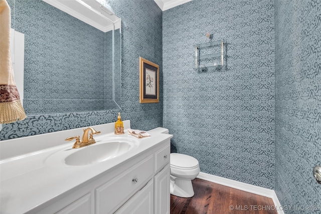 half bathroom featuring toilet, wood finished floors, wallpapered walls, baseboards, and vanity