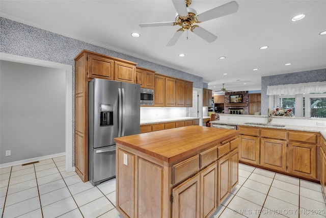 kitchen with butcher block countertops, a sink, a center island, stainless steel appliances, and ceiling fan