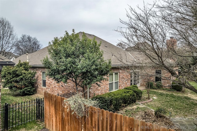 view of side of home featuring brick siding, a shingled roof, a chimney, and fence