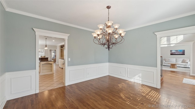 unfurnished room featuring a wealth of natural light, an inviting chandelier, wood finished floors, and crown molding