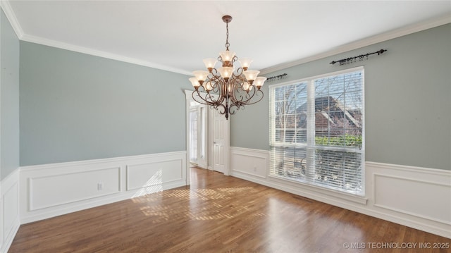 unfurnished dining area featuring an inviting chandelier, wood finished floors, a wainscoted wall, and ornamental molding