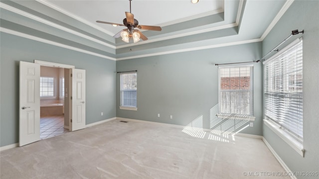 carpeted spare room featuring ceiling fan, a tray ceiling, baseboards, and ornamental molding