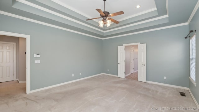 unfurnished bedroom featuring visible vents, crown molding, baseboards, a tray ceiling, and carpet floors