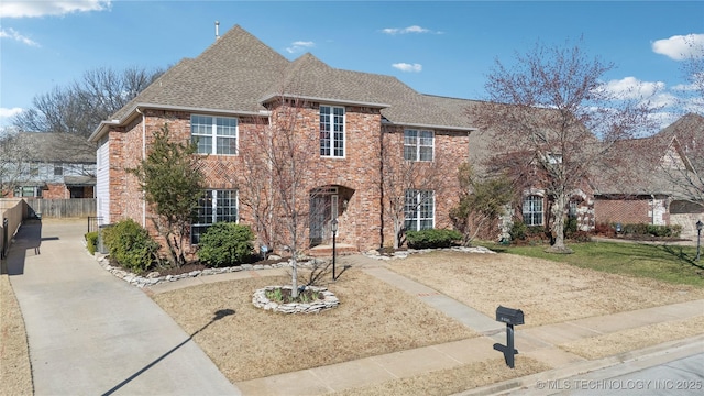 traditional home featuring fence, brick siding, and roof with shingles