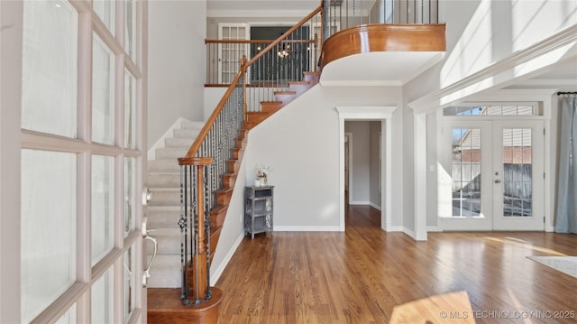 foyer featuring ornamental molding, wood finished floors, french doors, a towering ceiling, and stairs