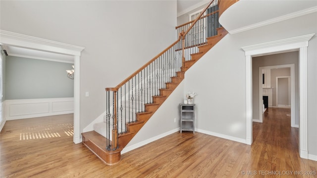 stairs featuring a chandelier, ornamental molding, wainscoting, and wood finished floors