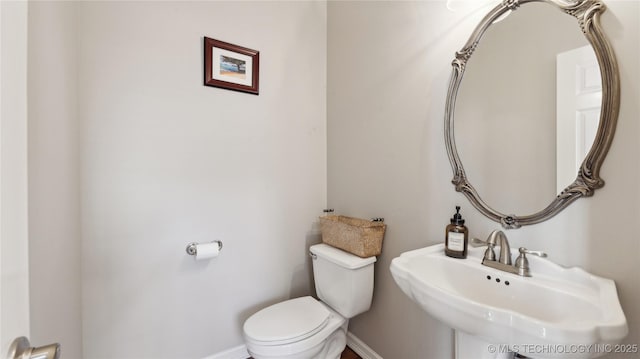 half bathroom with a sink, baseboards, and toilet