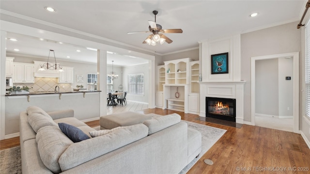 living area featuring ceiling fan with notable chandelier, crown molding, wood finished floors, and a fireplace