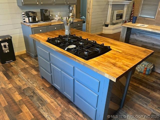 kitchen featuring wooden walls, dark wood finished floors, blue cabinetry, black gas stovetop, and butcher block counters