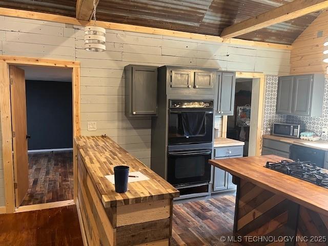 kitchen with wooden walls, dark wood finished floors, lofted ceiling with beams, black appliances, and wood counters