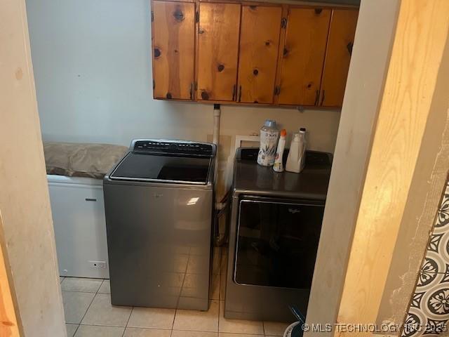 clothes washing area featuring light tile patterned floors, cabinet space, and washer and dryer