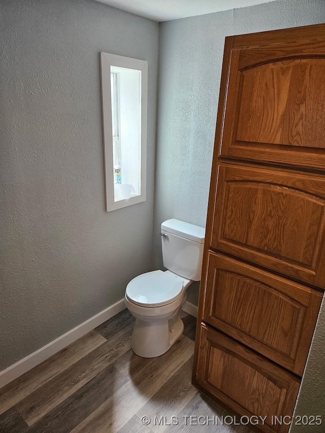bathroom featuring baseboards, toilet, a textured wall, and wood finished floors