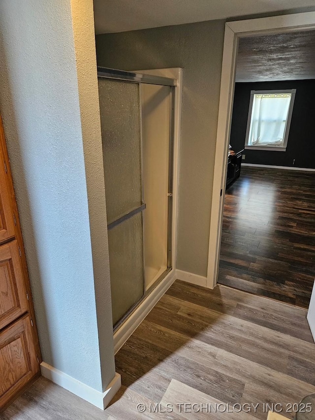 bathroom with baseboards, wood finished floors, a stall shower, and a textured wall