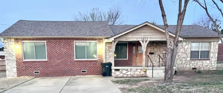 view of front of home with crawl space, stone siding, brick siding, and a porch