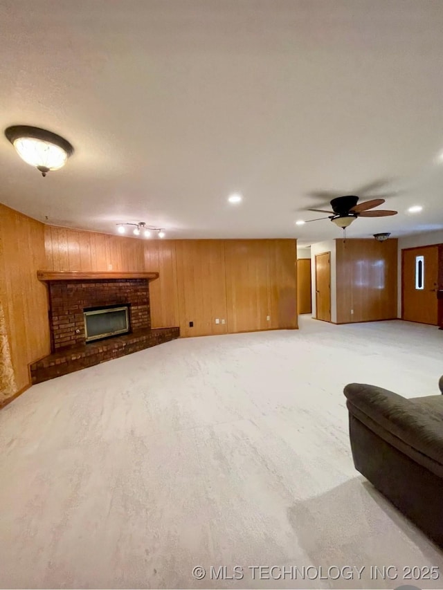 unfurnished living room featuring light carpet, a ceiling fan, wood walls, and a fireplace