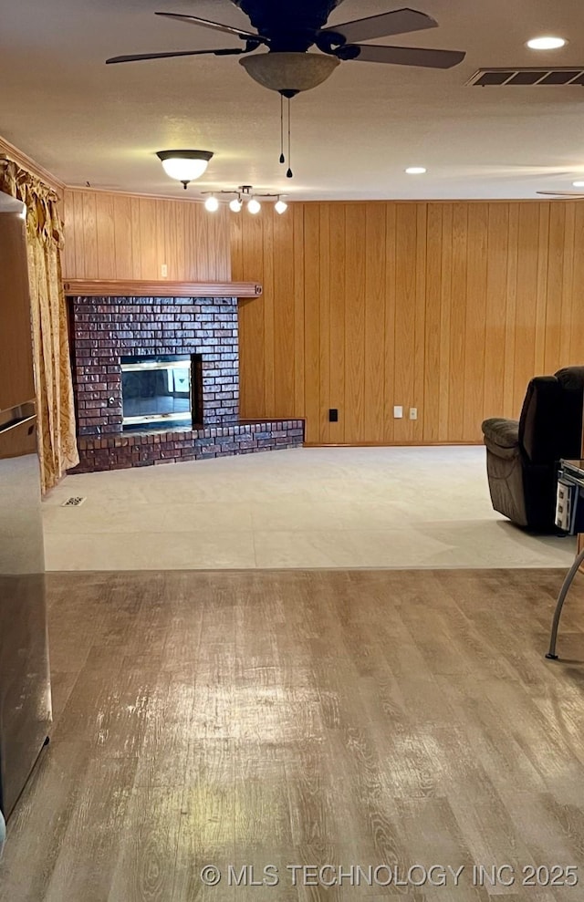 unfurnished living room featuring visible vents, wood walls, a fireplace, and a ceiling fan