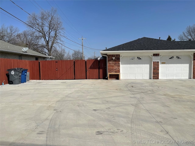 view of property exterior featuring a gate, an attached garage, concrete driveway, and fence