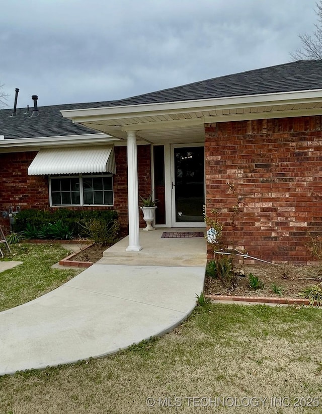 doorway to property with brick siding and a shingled roof