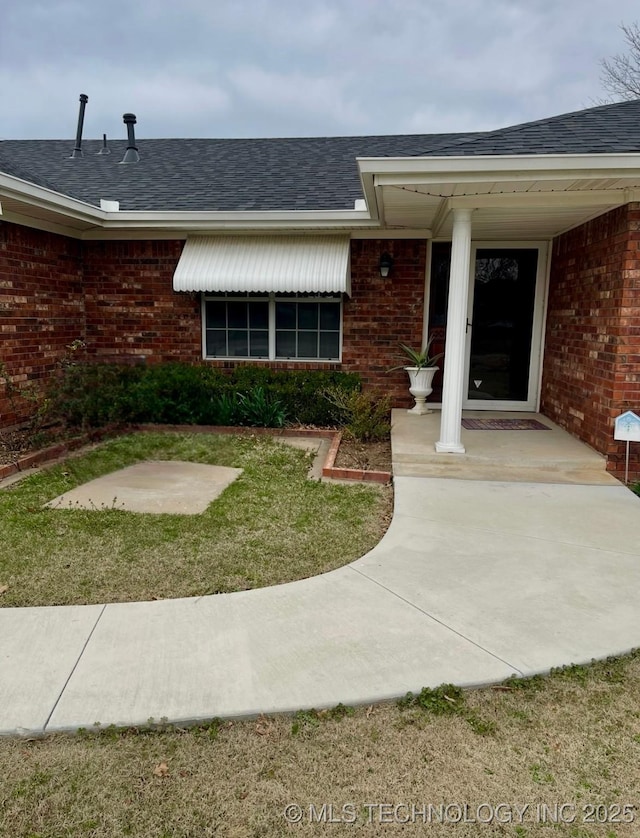 view of exterior entry featuring brick siding and roof with shingles