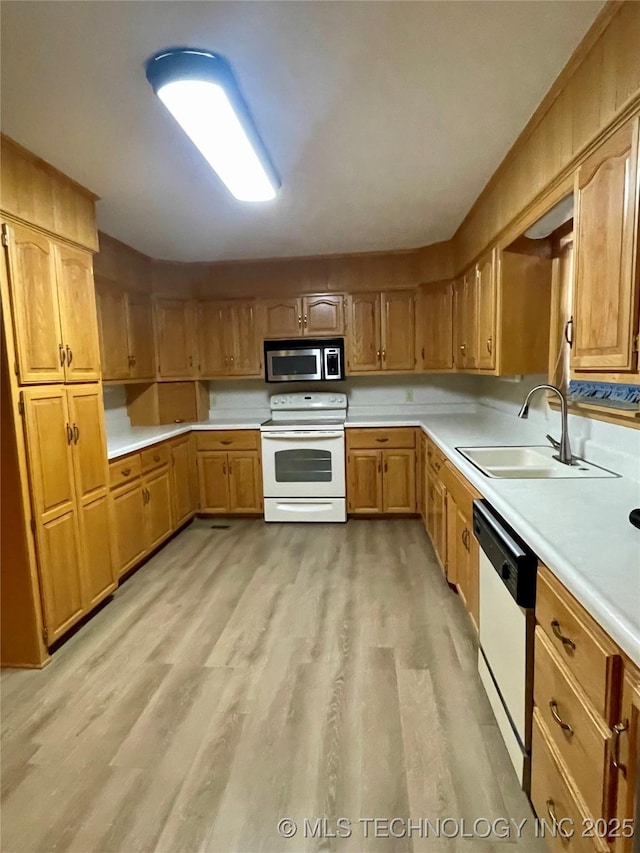 kitchen featuring white appliances, light countertops, light wood-style floors, and a sink