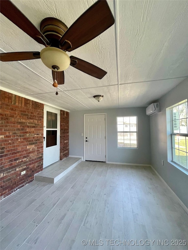 interior space with wood finished floors, baseboards, brick wall, a wall mounted AC, and a textured ceiling