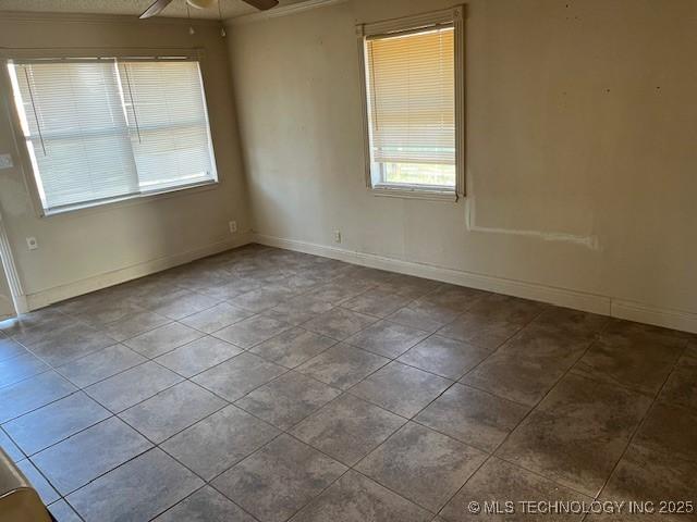 tiled empty room featuring a ceiling fan and baseboards