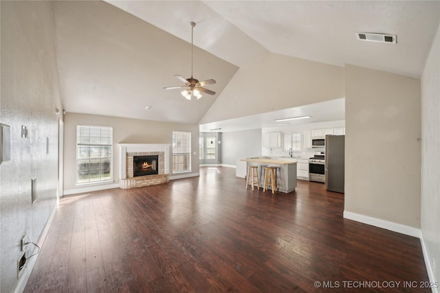 unfurnished living room with visible vents, high vaulted ceiling, dark wood finished floors, ceiling fan, and a brick fireplace