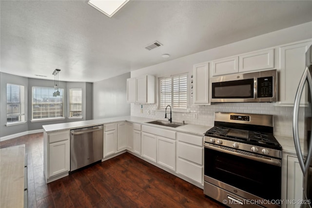 kitchen featuring visible vents, a peninsula, dark wood-style floors, stainless steel appliances, and a sink