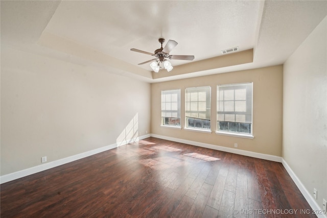 spare room with a raised ceiling, wood finished floors, visible vents, and baseboards