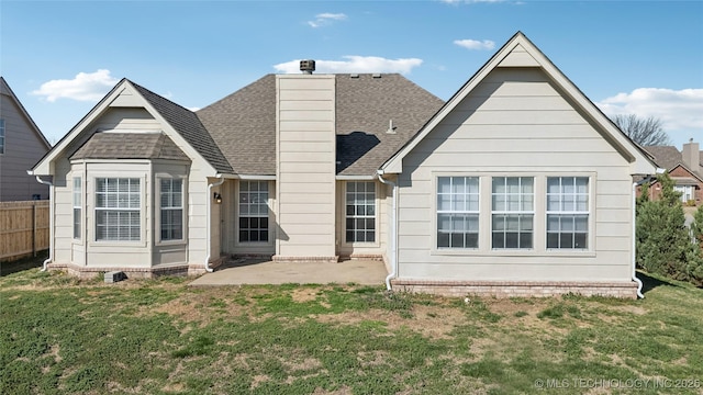 back of house with a lawn, a patio, fence, a shingled roof, and a chimney