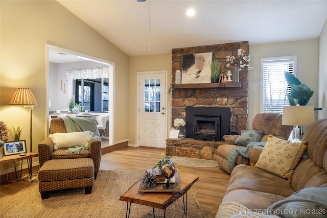 living room featuring baseboards, a stone fireplace, wood finished floors, and vaulted ceiling