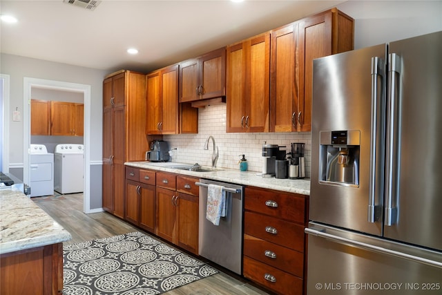 kitchen featuring brown cabinetry, a sink, decorative backsplash, appliances with stainless steel finishes, and washer and clothes dryer