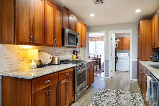 kitchen featuring visible vents, light stone counters, washer / clothes dryer, backsplash, and appliances with stainless steel finishes