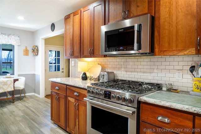 kitchen featuring stainless steel appliances, light stone countertops, backsplash, and brown cabinetry