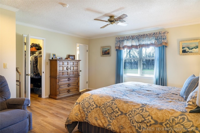 bedroom featuring light wood-type flooring, a textured ceiling, a spacious closet, and crown molding