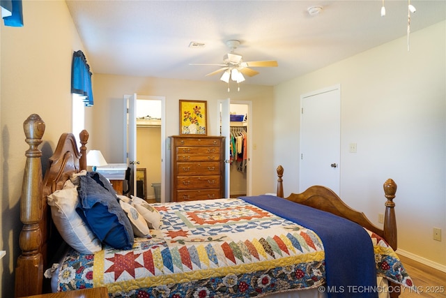 bedroom with a walk in closet, visible vents, wood finished floors, a closet, and ceiling fan