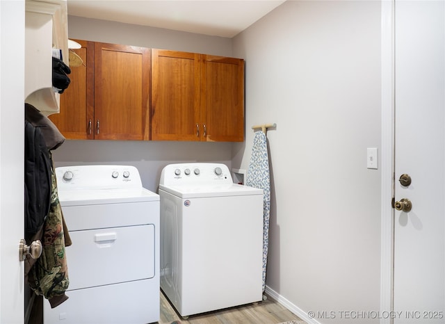 laundry room with light wood-style flooring, cabinet space, baseboards, and washing machine and clothes dryer