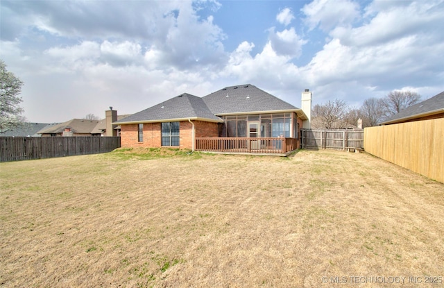 back of property with brick siding, roof with shingles, a chimney, a fenced backyard, and a yard